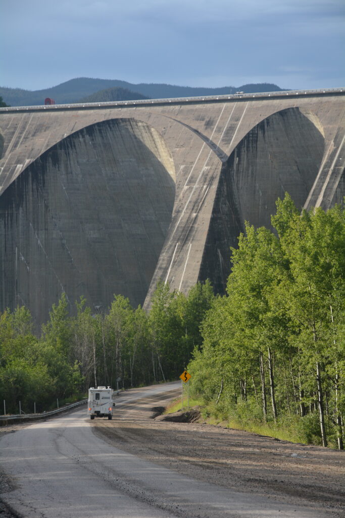 A wide angle shot of a truck with a truck camper travelling down a long windy gravel road towards the massive hydroelectric structure in Manic 5, Quebec Canada. 