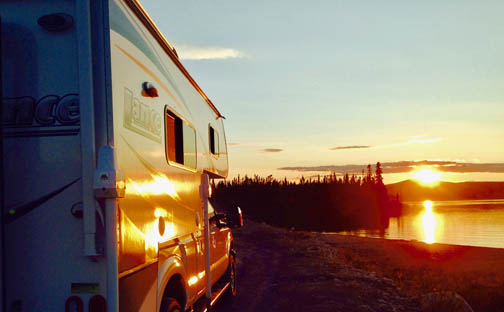 Lance 825 on a white Ford F-250 boondocks on a deserted beach during sundown. The orange and red light beautifully reflects off the side of the vehicle and the water in the backround.