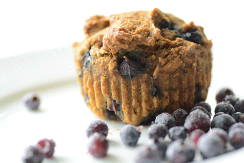 A golden blueberry oat muffin sits on a place with purple frosted wild blueberries
