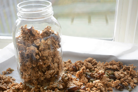 Mason jar filled with homemade allergen-free granola sitting atop a baking pan with granola spread out onto it.