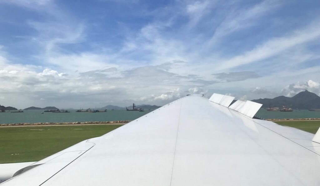 View from a landed plane window looking out onto the wing. In the background there is blue sky with fluffy clouds.
