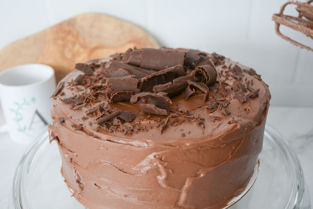 A close up shot of a gluten free vegan chocolate cake topped with chocolate icing and curls.