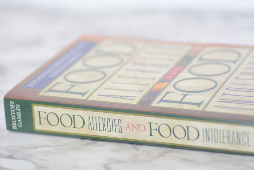 A photo of the textbook "Food Allergies and Food Intolerance" by Brostoff Gamlin sits on its side on a white marble countertop.