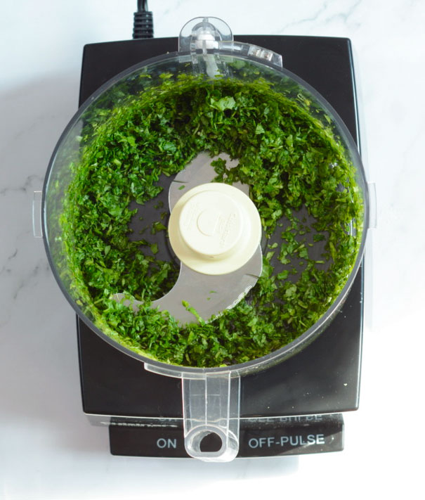An overhead view of chopped fresh basil and baby spinach leaves in a cuisinart food processor sitting on a white countertop.